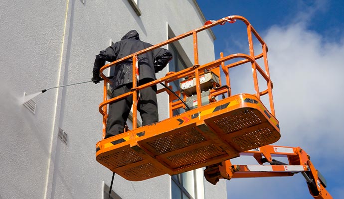Worker power washing a building from a boom lift Worker power washing a building from a boom lift